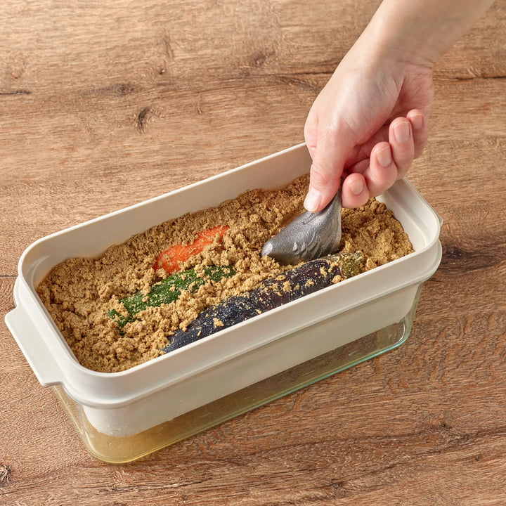 Person placing a bird shaped cast iron supplement into a Japanese nukazoko rice bran pickling box on wooden table