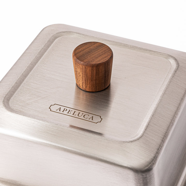Close up view of wooden knob and Apeluca logo engraved on stainless steel lid of Japanese carbon steel pan
