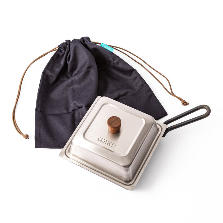 Japanese Luxe Carbon Steel Deep Pan with lid displayed next to its black fabric storage pouch on white background