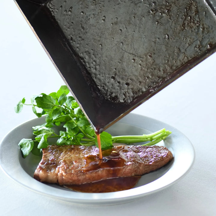 Pouring pan sauce smoothly from the corner of a square compact deep frying pan onto a cooked steak