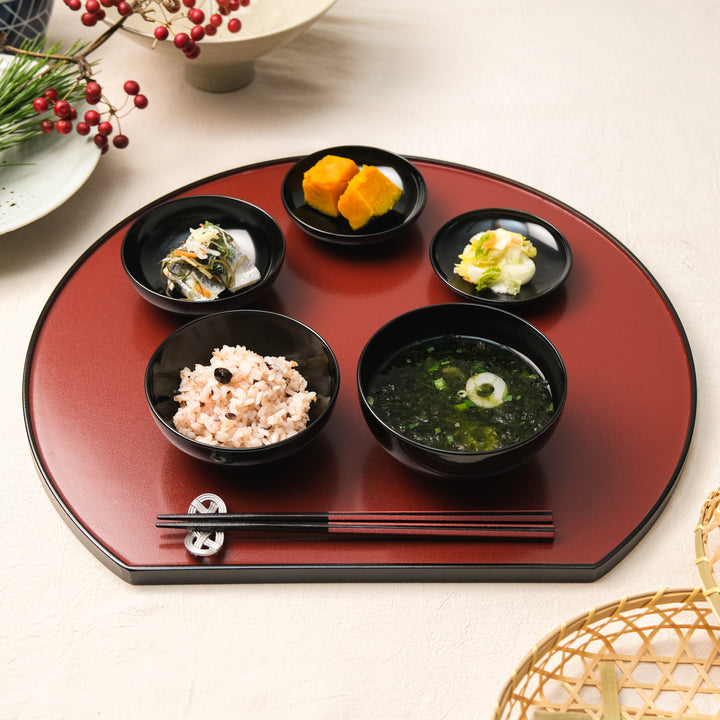 Japanese lacquer serving tray with black bowls holding rice soup and seasonal side dishes arranged for a traditional meal