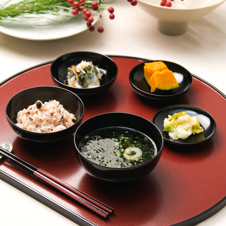 Japanese lacquer tray with black bowls serving rice soup, multigrain rice, and seasonal side dishes