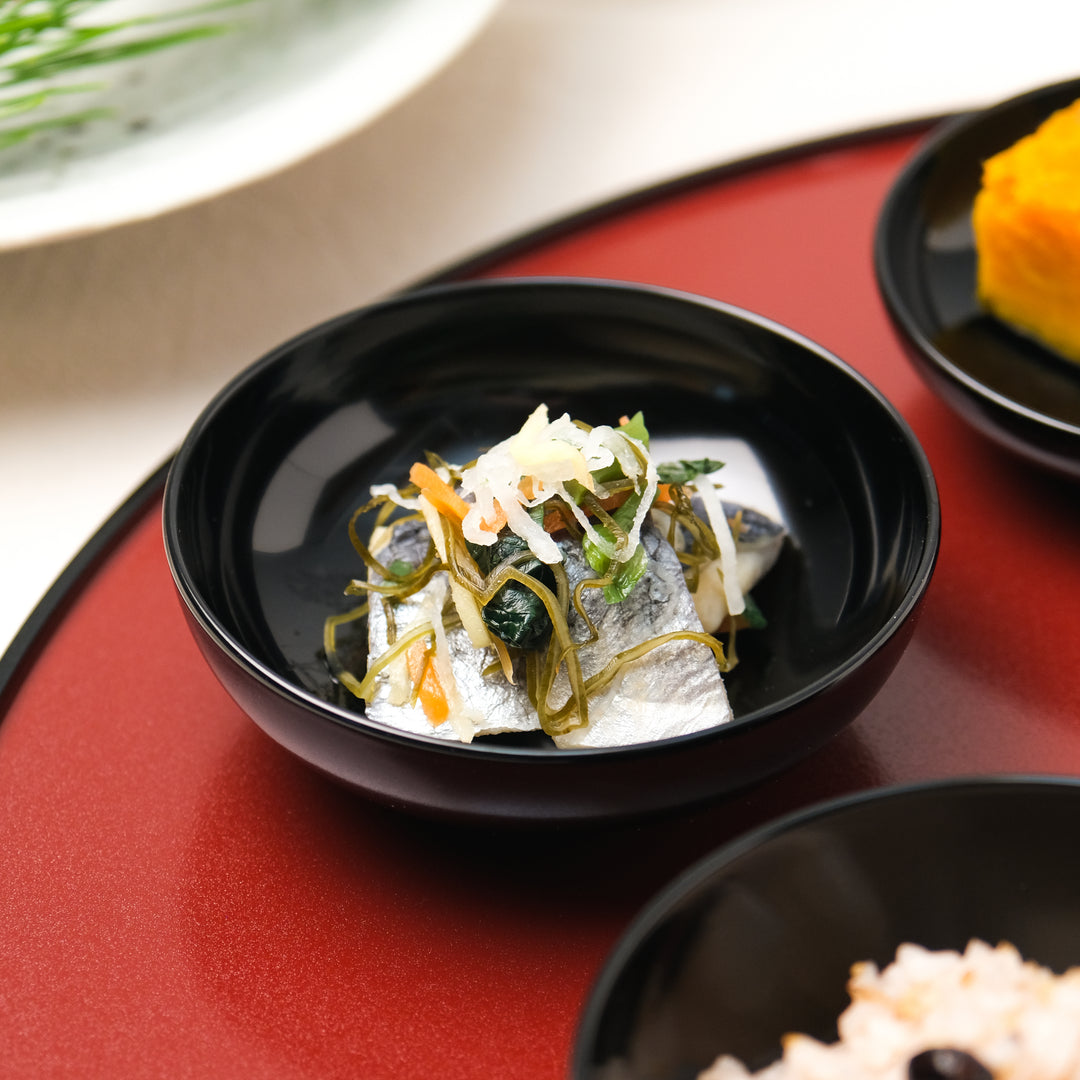 Black lacquer bowl holding a small Japanese side dish on a red lacquer tray