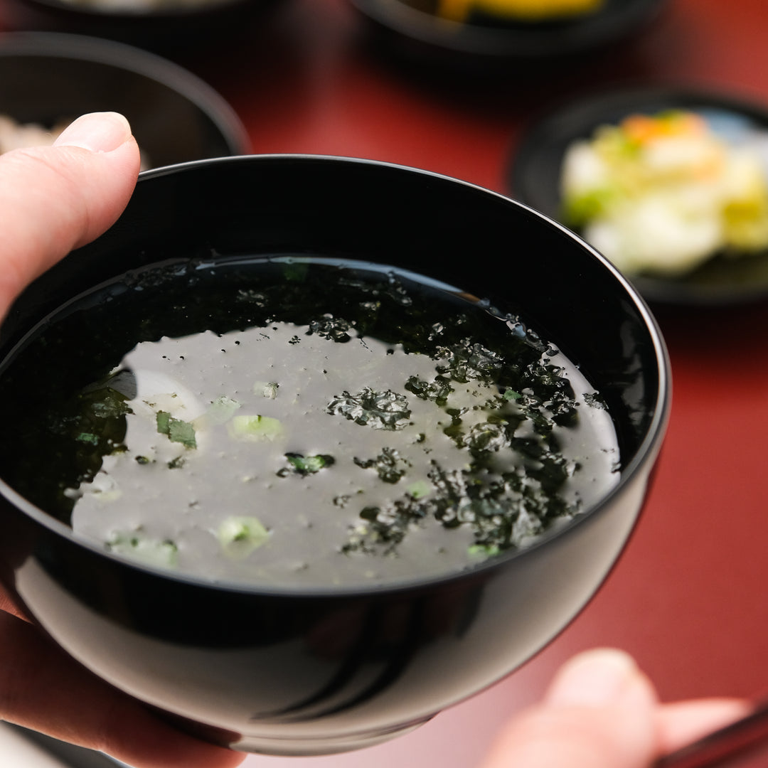 Black lacquer soup bowl held in hand with clear Japanese seaweed soup