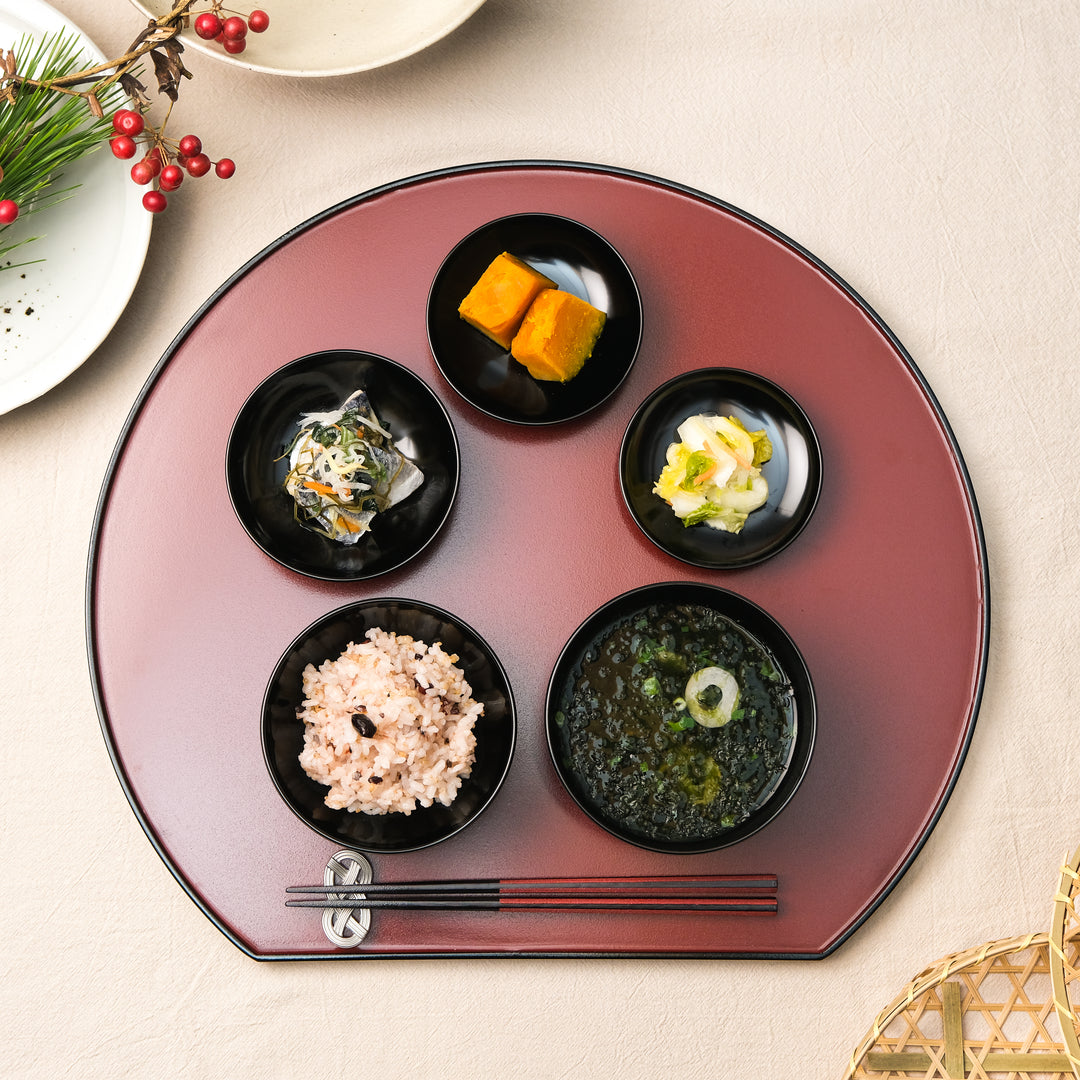 Japanese lacquer serving tray with small black bowls holding seasonal side dishes arranged for a traditional meal