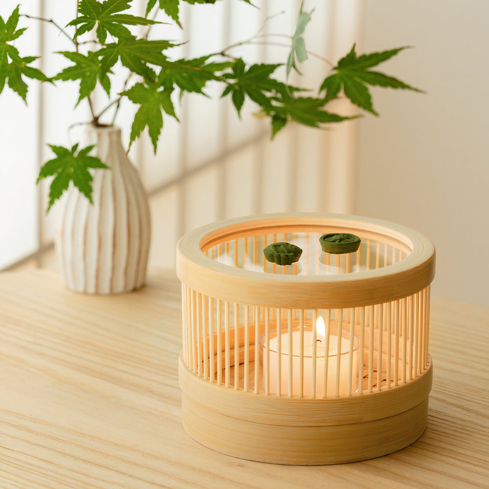 Side view of a handcrafted bamboo incense burner showing delicate wooden slats with a glowing candle inside