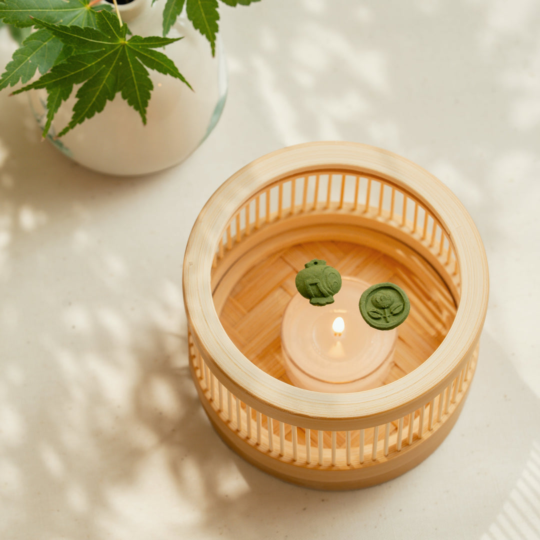 Top view of a round bamboo incense warmer with tea motif green matcha pressed incense and a lit candle