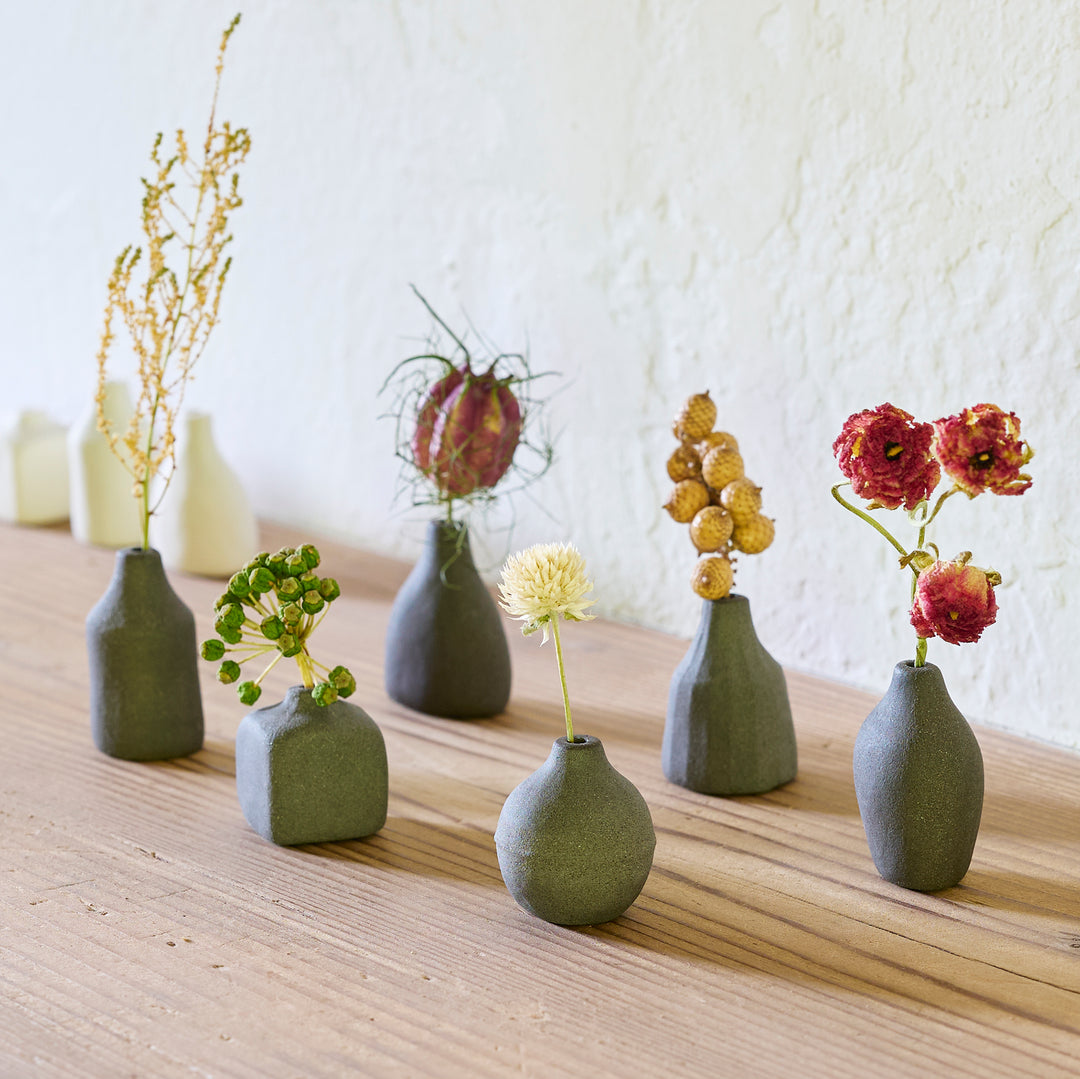Black minimalist ceramic bud vases in geometric shapes on wooden table displaying dried wildflowers for home decor