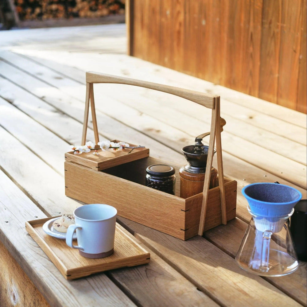 Japanese wooden okamochi storage caddy with removable trays used outdoors for coffee setup with dripper and mug