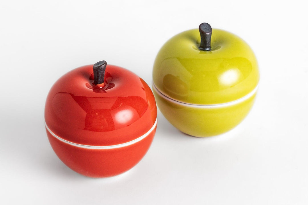 Glossy apple shaped containers in red and green with dark stems, designed for playful kitchen or table storage.