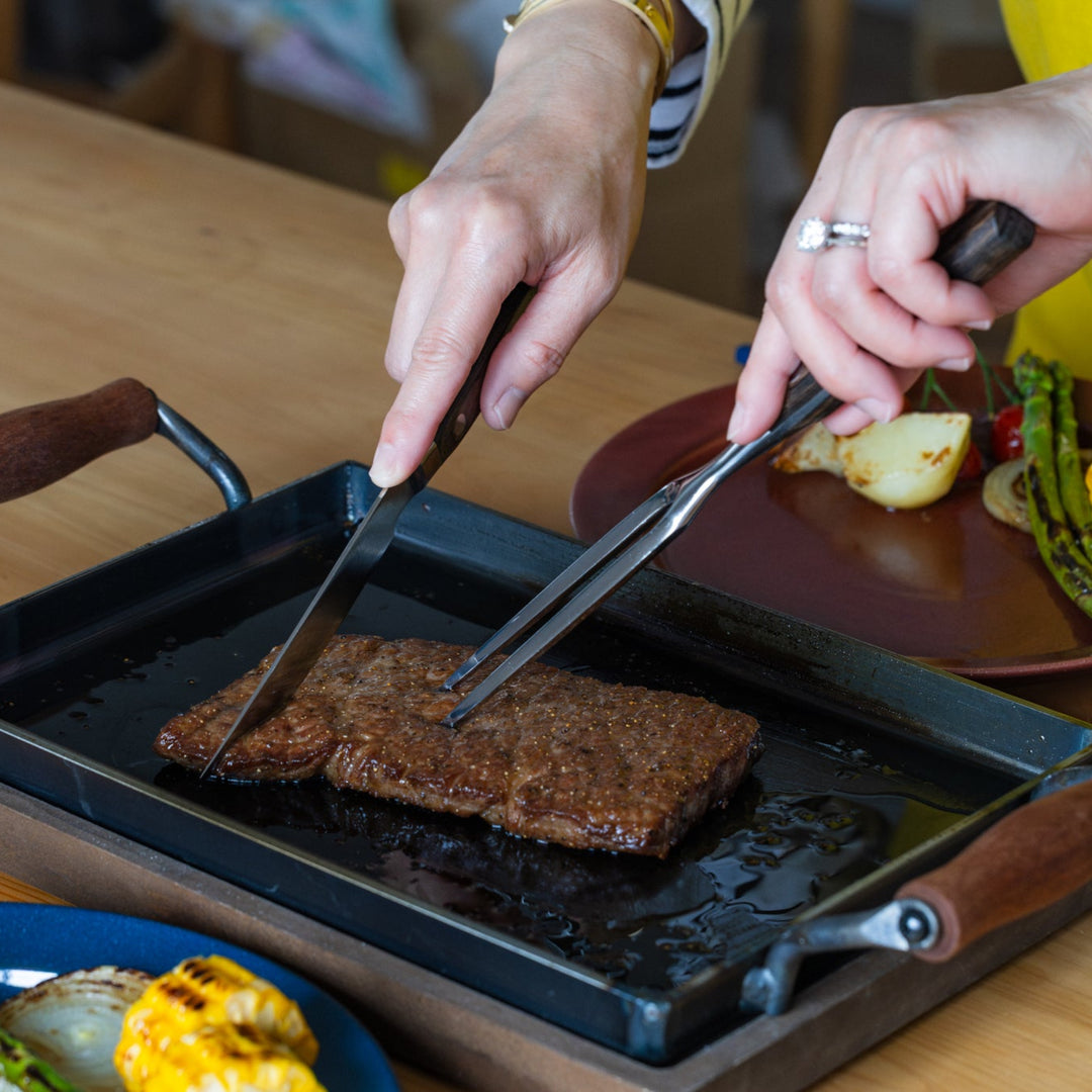 Nami cutting grilled steak using japanese carving knife and fork on iron griddle plate barbecue kitchenware