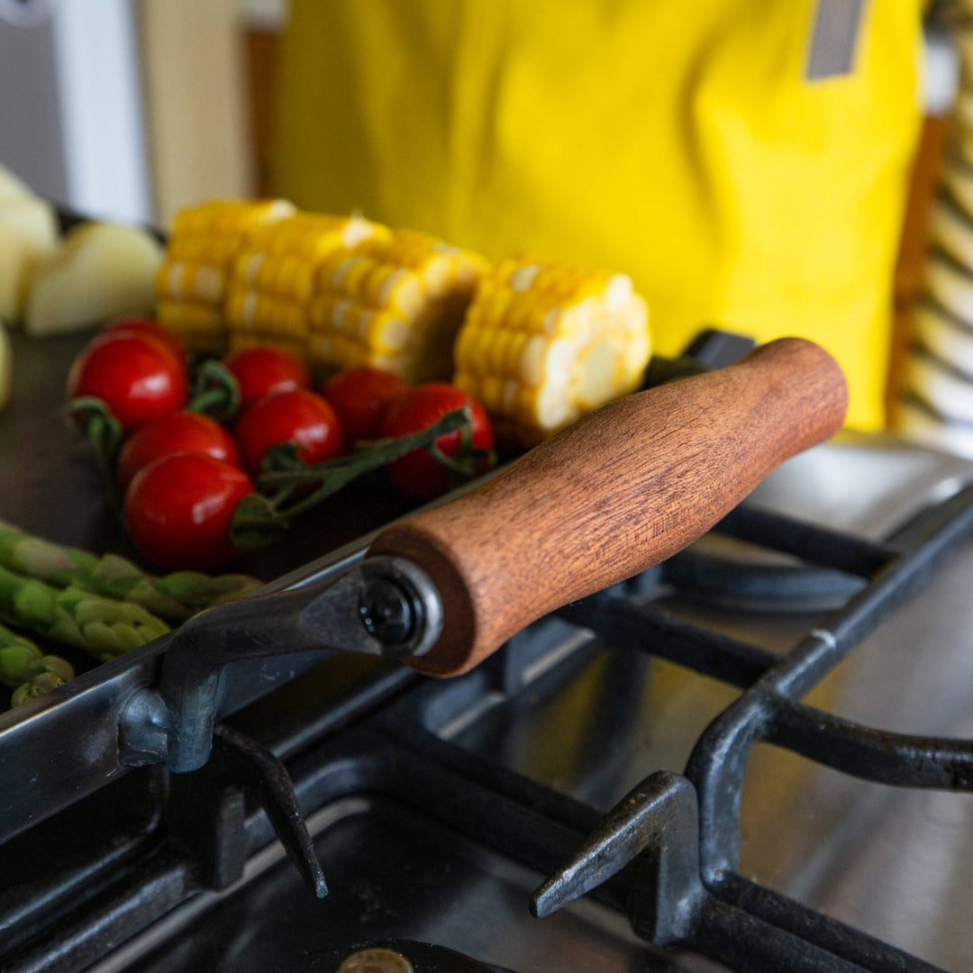 Wooden handle on aux japanese cast iron griddle with lid next to nami in yellow apron cooking stovetop bbq plate