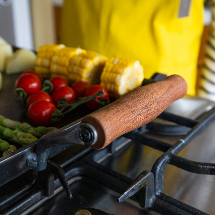 Wooden handle on aux japanese cast iron griddle with lid next to nami in yellow apron cooking stovetop bbq plate