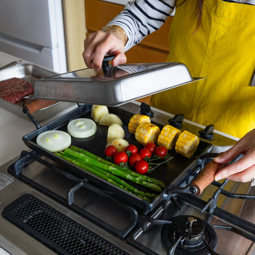 Nami lifting metal lid of aux japanese cast iron griddle with lid cooking fresh vegetables on gas stove hot plate
