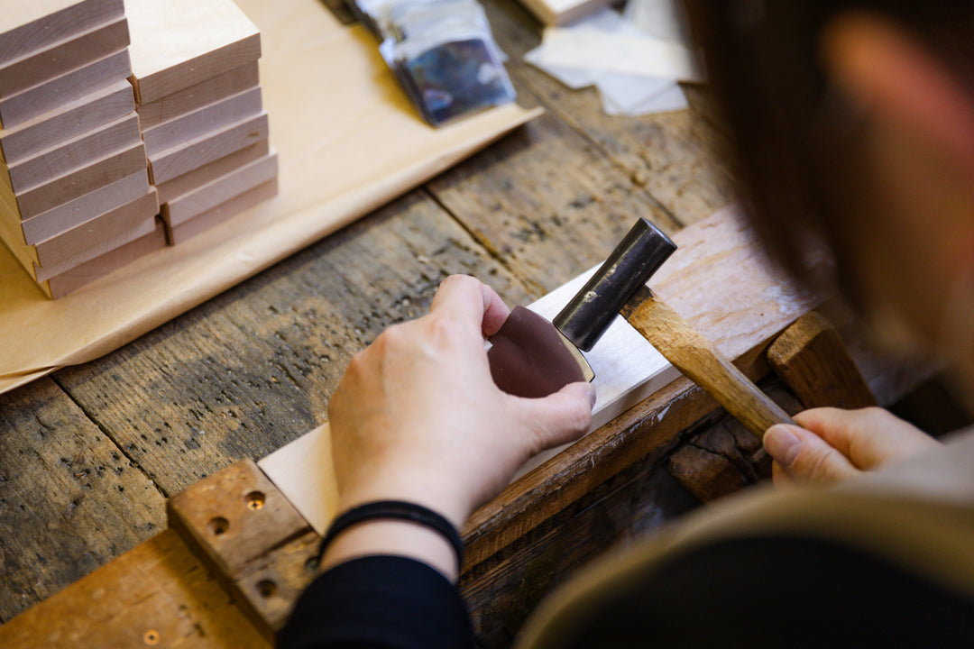Craftsperson shaping a wooden piece by hand with a small plane, refining the surface on a rustic workbench.