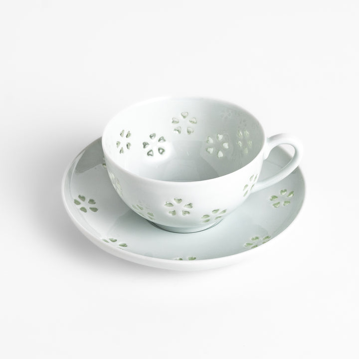 Delicate teacup and saucer set featuring intricate petal-shaped cutouts, allowing light to pass through, creating a soft, elegant design in pale green and white porcelain.
