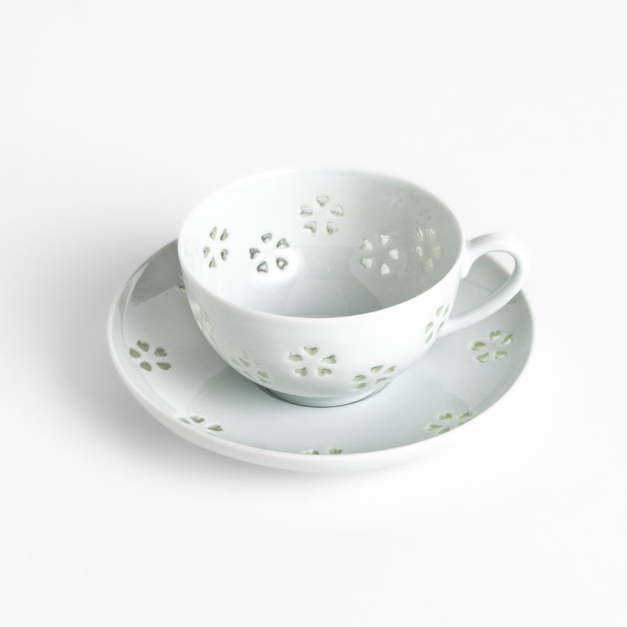 Delicate teacup and saucer set featuring intricate petal-shaped cutouts, allowing light to pass through, creating a soft, elegant design in pale green and white porcelain.