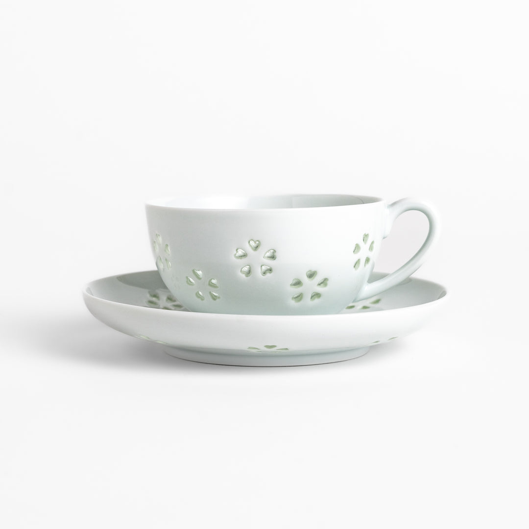 Delicate teacup and saucer set featuring intricate petal-shaped cutouts, allowing light to pass through, creating a soft, elegant design in pale green and white porcelain.