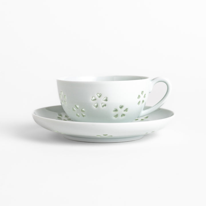 Delicate teacup and saucer set featuring intricate petal-shaped cutouts, allowing light to pass through, creating a soft, elegant design in pale green and white porcelain.