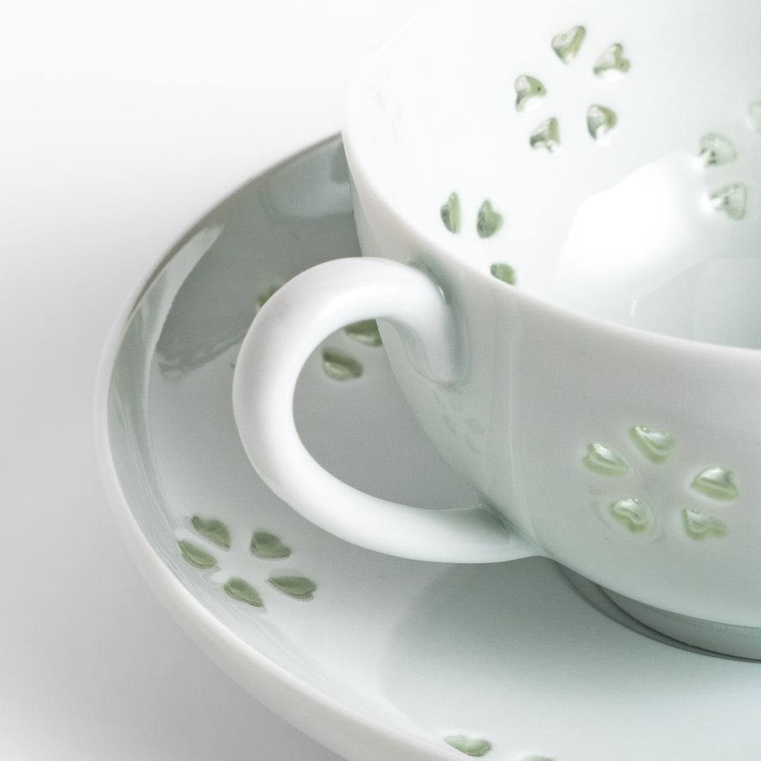 Delicate teacup and saucer set featuring intricate petal-shaped cutouts, allowing light to pass through, creating a soft, elegant design in pale green and white porcelain.