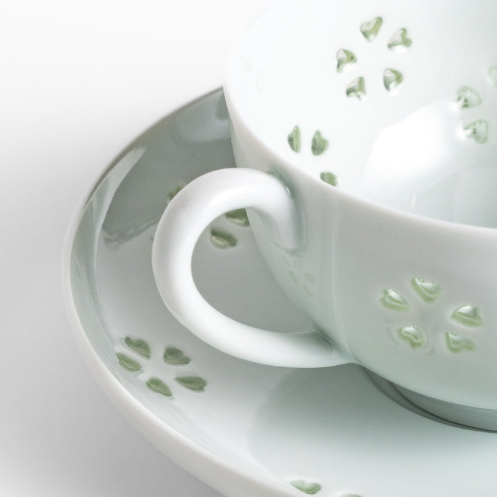 Delicate teacup and saucer set featuring intricate petal-shaped cutouts, allowing light to pass through, creating a soft, elegant design in pale green and white porcelain.