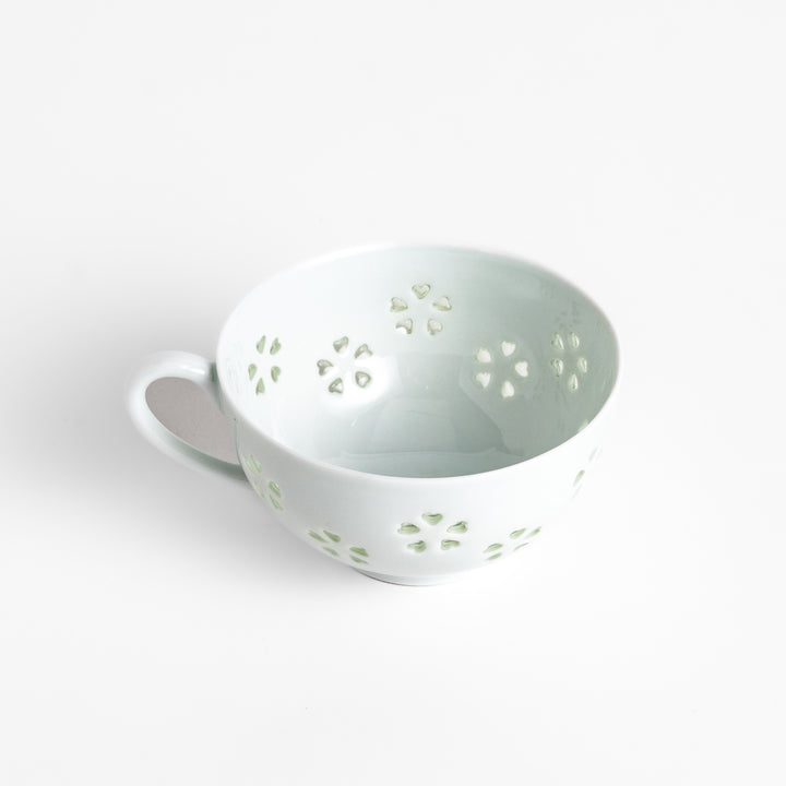 Delicate teacup and saucer set featuring intricate petal-shaped cutouts, allowing light to pass through, creating a soft, elegant design in pale green and white porcelain.