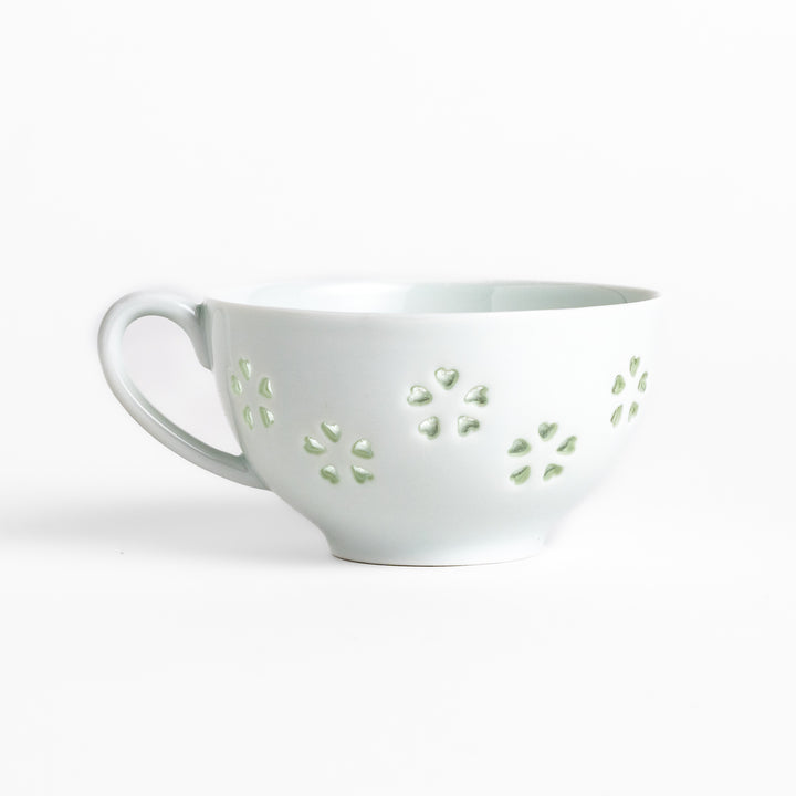 Delicate teacup and saucer set featuring intricate petal-shaped cutouts, allowing light to pass through, creating a soft, elegant design in pale green and white porcelain.