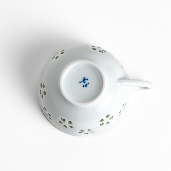 Delicate teacup and saucer set featuring intricate petal-shaped cutouts, allowing light to pass through, creating a soft, elegant design in pale green and white porcelain.