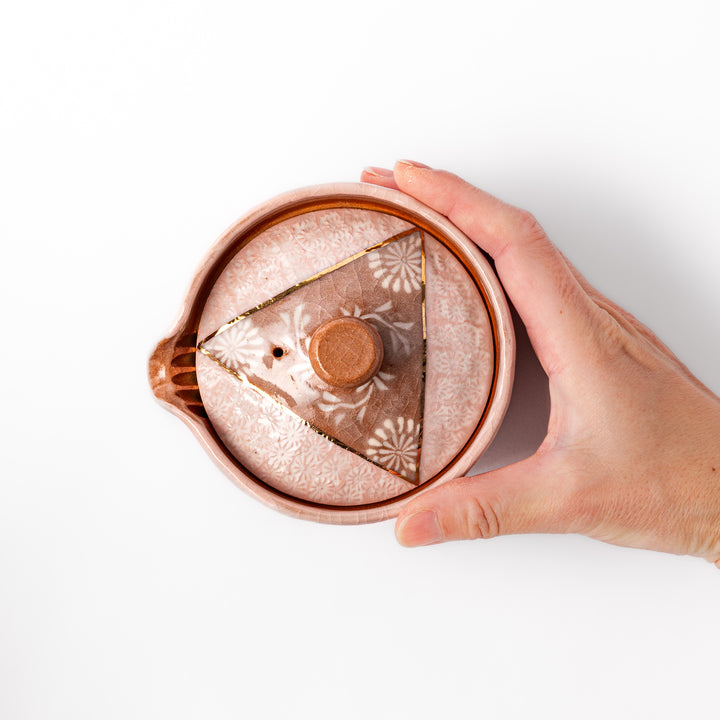 Ceramic teapot with a soft pink crackled glaze, floral patterns, and a curved spout accented by a hand-applied gold line for an artisanal touch.