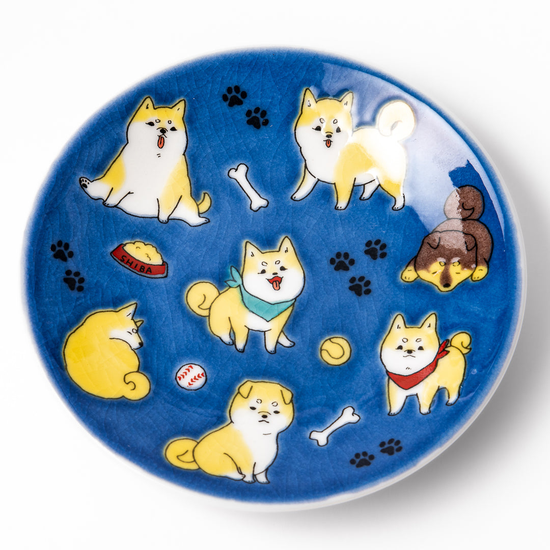 Round Japanese ceramic sauce dish with a deep blue background decorated with playful Shiba Inu dogs, paw prints, and bones, perfect for condiments or snacks.