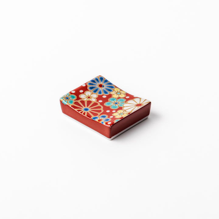 Rectangular Japanese ceramic chopstick rest with a red background decorated with colorful plum and chrysanthemum blossoms, perfect for elegant dining settings.