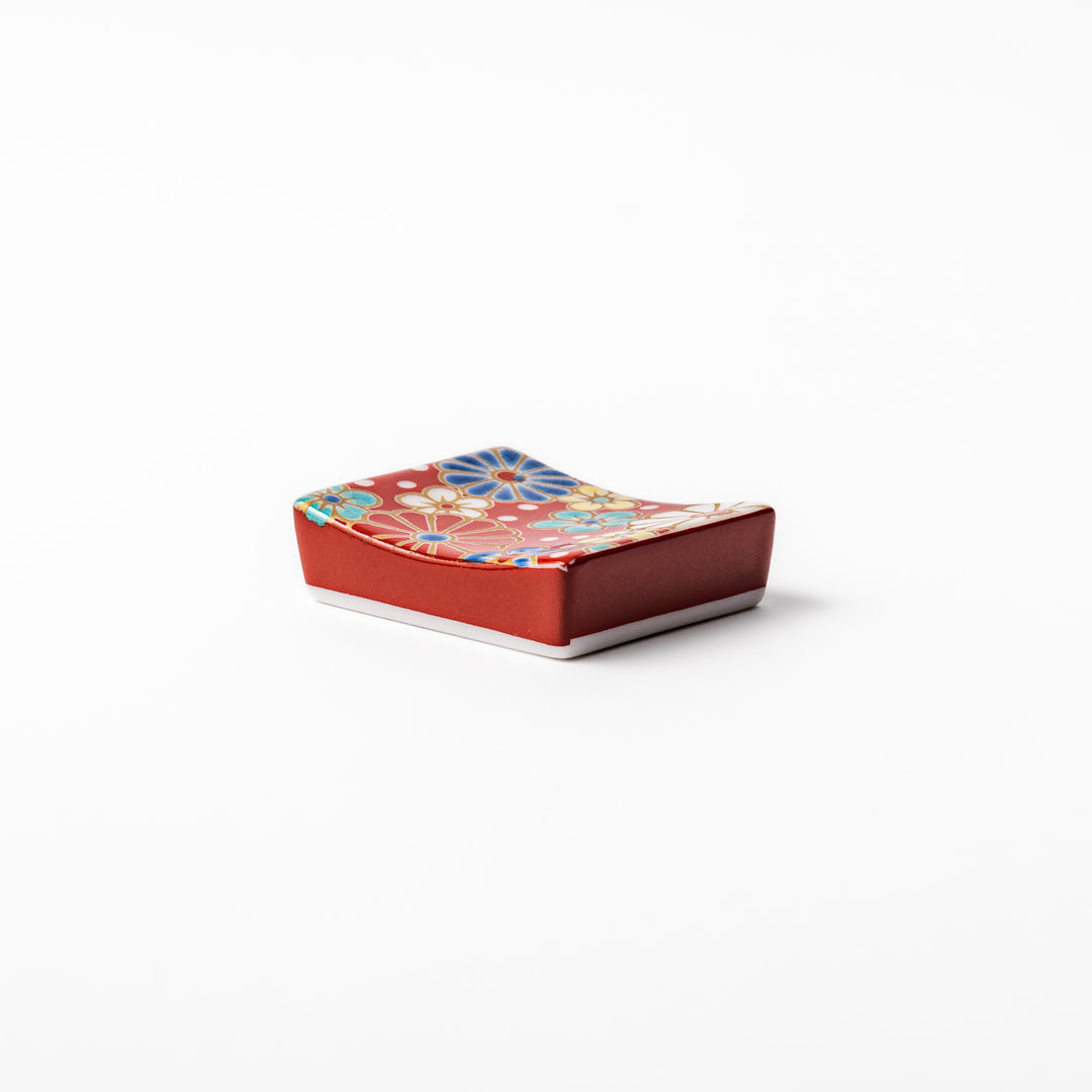 Rectangular Japanese ceramic chopstick rest with a red background decorated with colorful plum and chrysanthemum blossoms, perfect for elegant dining settings.
