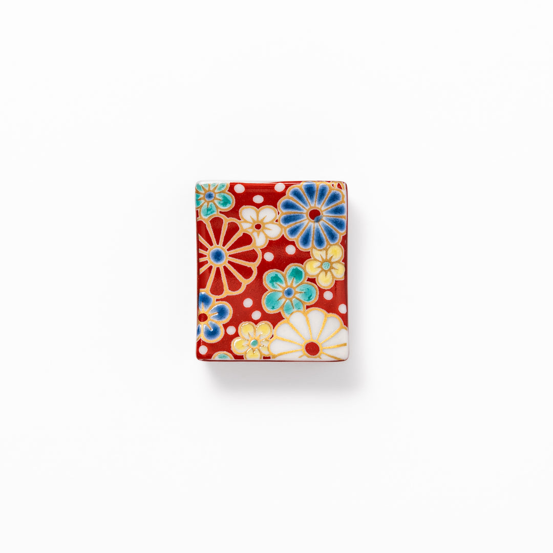 Rectangular Japanese ceramic chopstick rest with a red background decorated with colorful plum and chrysanthemum blossoms, perfect for elegant dining settings.