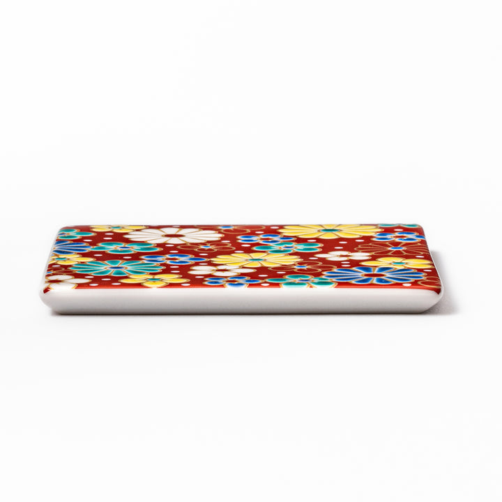 Square Japanese ceramic coaster with a red background decorated with colorful plum and chrysanthemum blossoms, adding elegance and tradition to table settings.