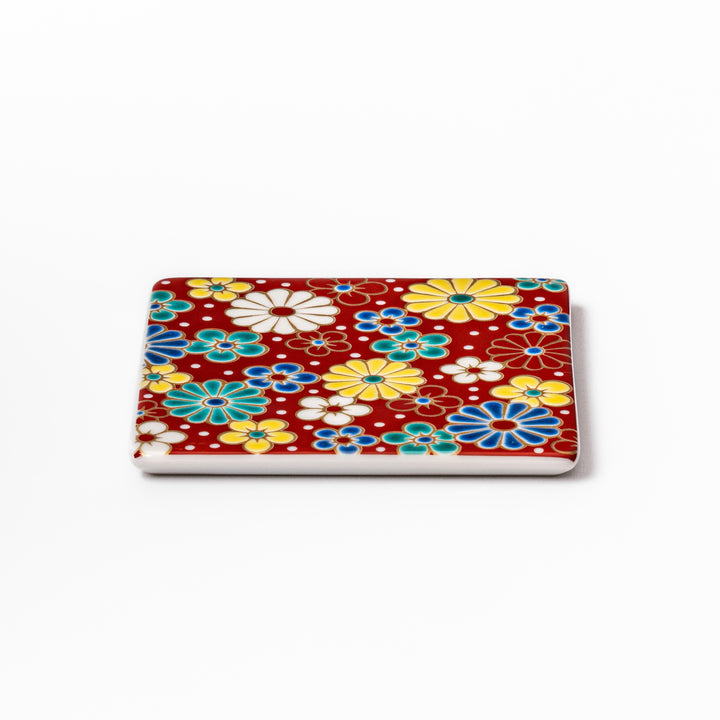 Square Japanese ceramic coaster with a red background decorated with colorful plum and chrysanthemum blossoms, adding elegance and tradition to table settings.