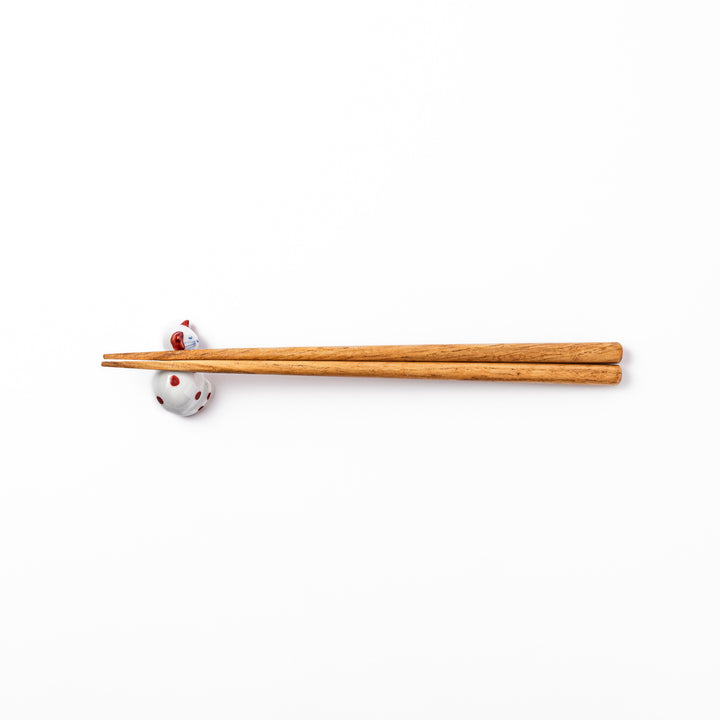 Red polka-dot ceramic cat chopstick rest in a sleeping pose, featuring hand-painted details and a glossy finish to add playful charm to your table setting.