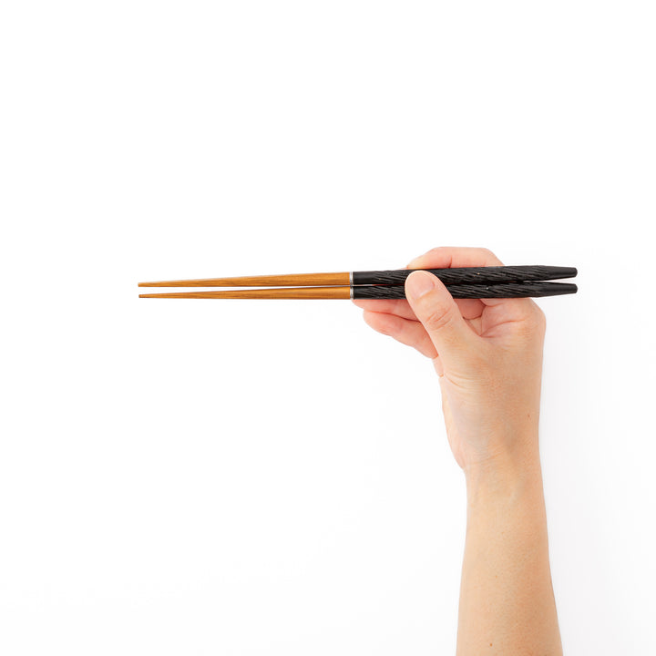 A hand holding black textured portable Japanese travel chopsticks showcasing a comfortable nonslip grip and standard length