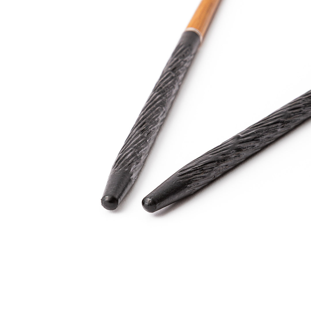 Portable Japanese travel chopsticks featuring a black textured handle with detailed carvings and a natural wood tip