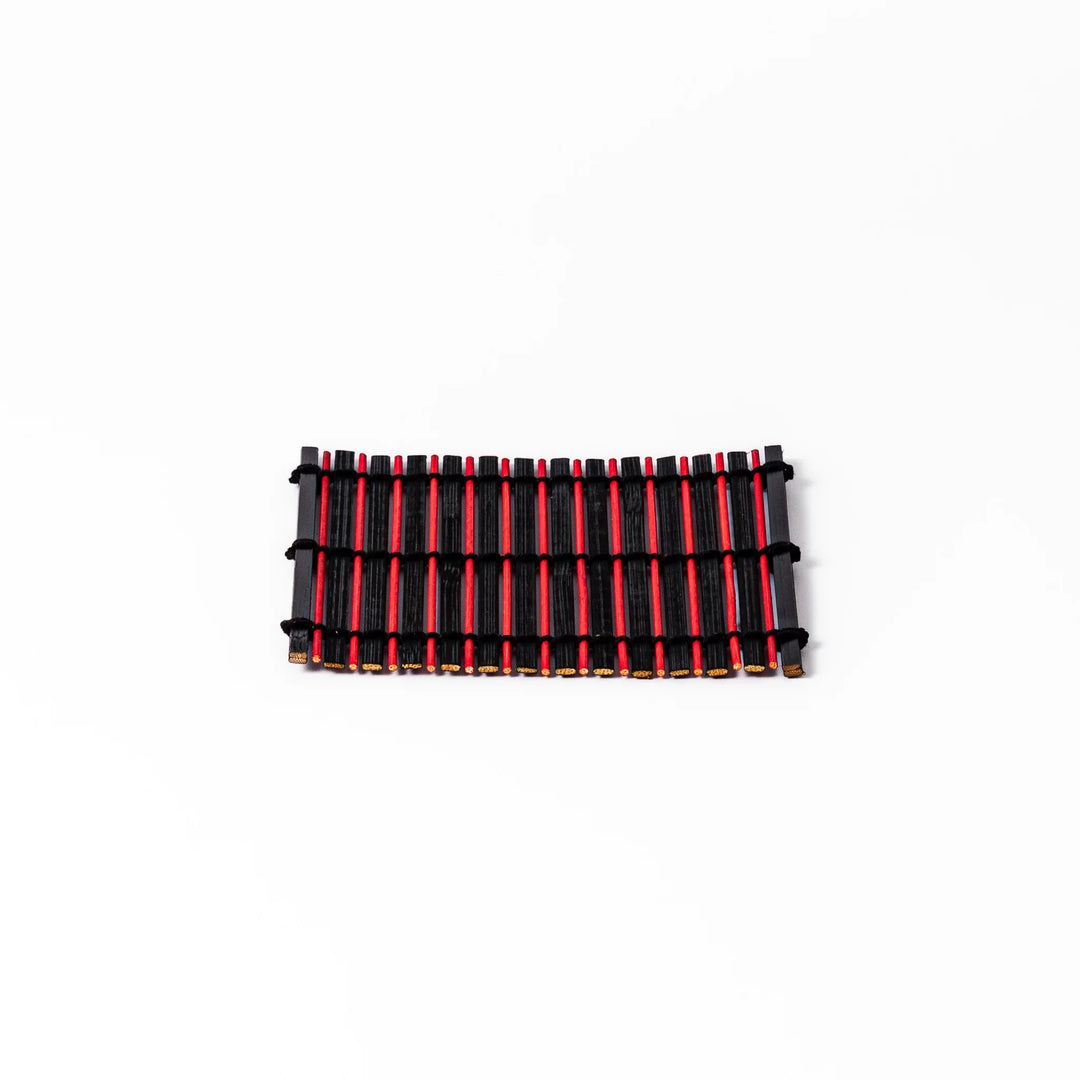 Red and black bamboo coaster with slim vertical slats and black cord ties, ideal for adding a striking accent to Japanese-style drink settings.
