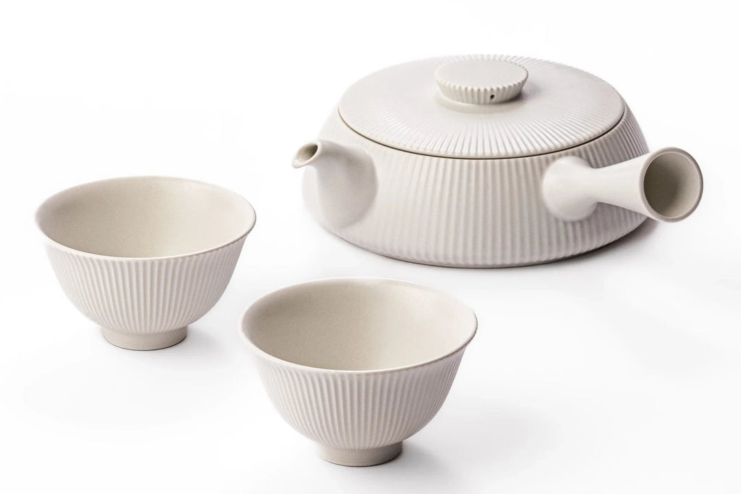 White porcelain kyusu teapot and two cups with subtle vertical ribbed texture sitting on a clean white background