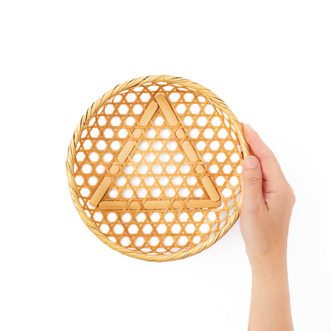 An open round handwoven bamboo serving basket with its hexagonal mesh pattern lid leaning slightly to the side