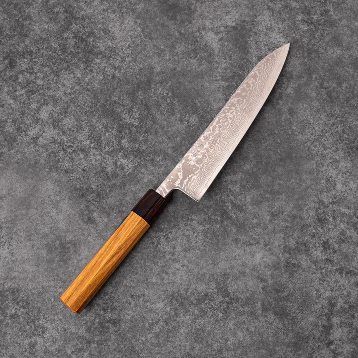 Japanese Damascus gyuto knife featuring a layered steel blade and natural wood handle displayed on gray stone background.