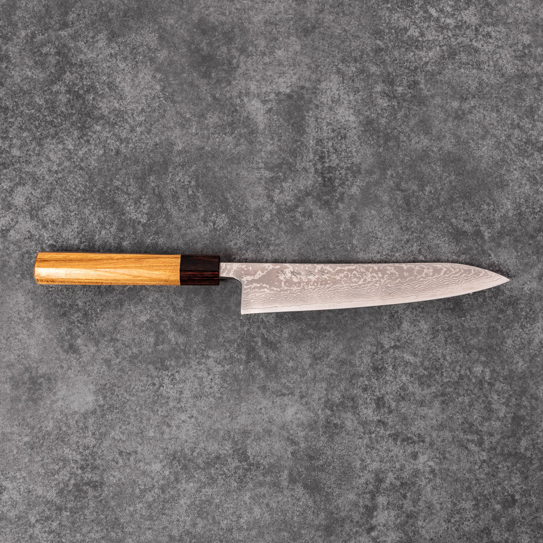 Japanese Damascus gyuto knife featuring a layered steel blade and natural wood handle displayed on gray stone background.