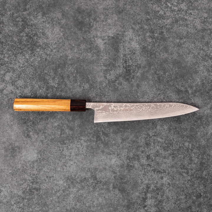 Japanese Damascus gyuto knife featuring a layered steel blade and natural wood handle displayed on gray stone background.