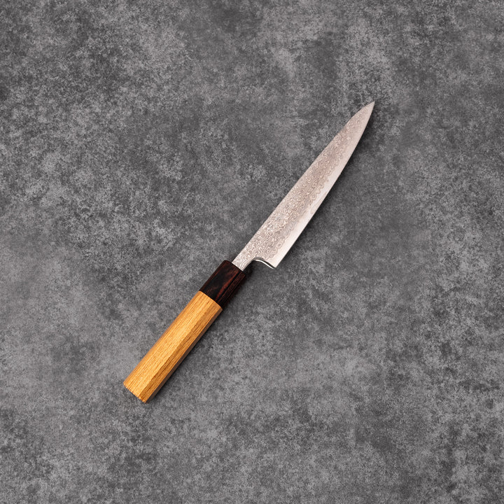 Japanese Damascus petty knife with intricate layered steel blade and natural wood handle placed on gray stone surface.