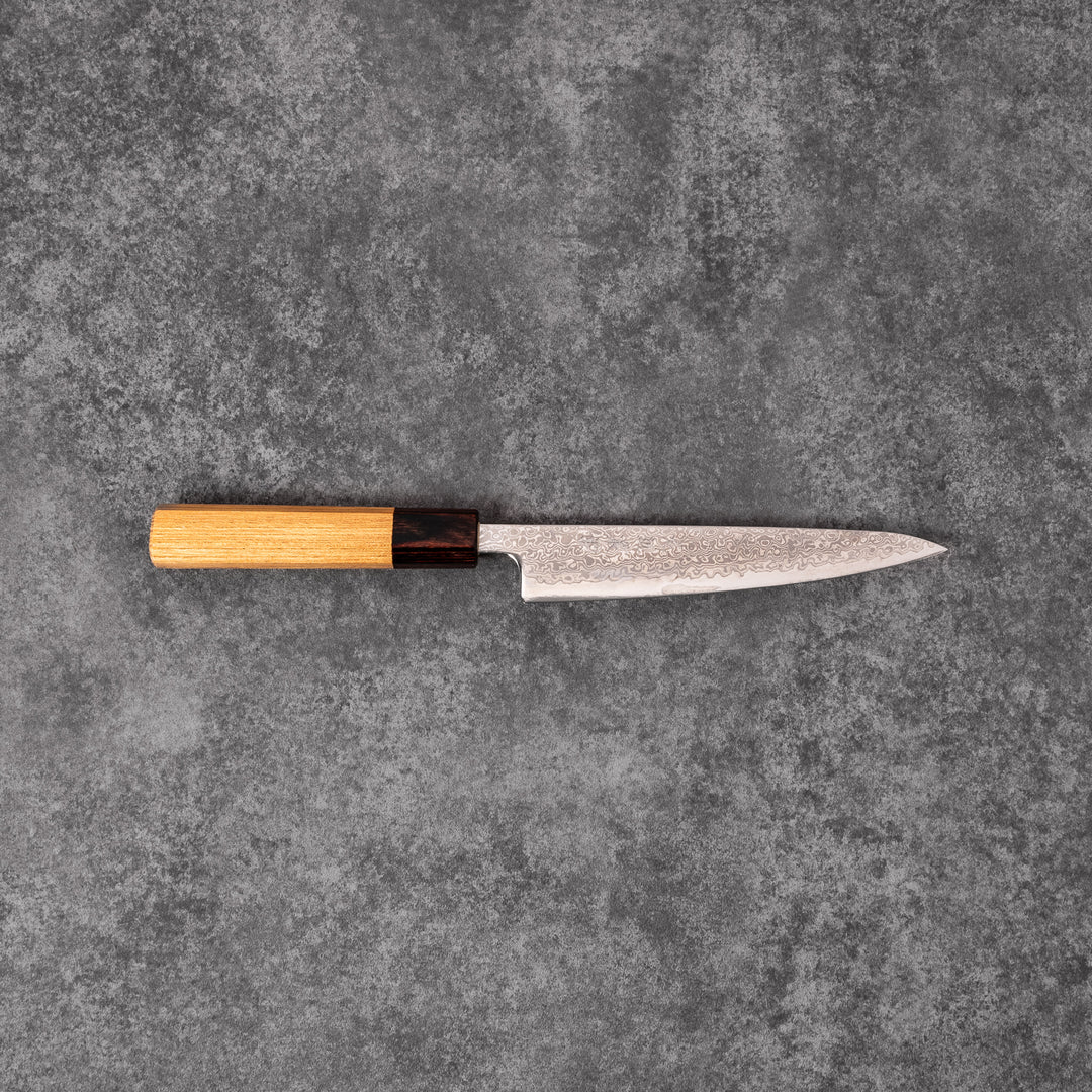 Japanese Damascus petty knife with intricate layered steel blade and natural wood handle placed on gray stone surface.