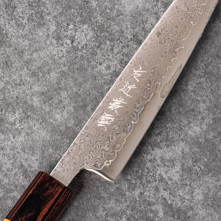 Japanese Damascus petty knife with intricate layered steel blade and natural wood handle placed on gray stone surface.