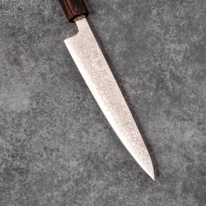 Japanese Damascus petty knife with intricate layered steel blade and natural wood handle placed on gray stone surface.