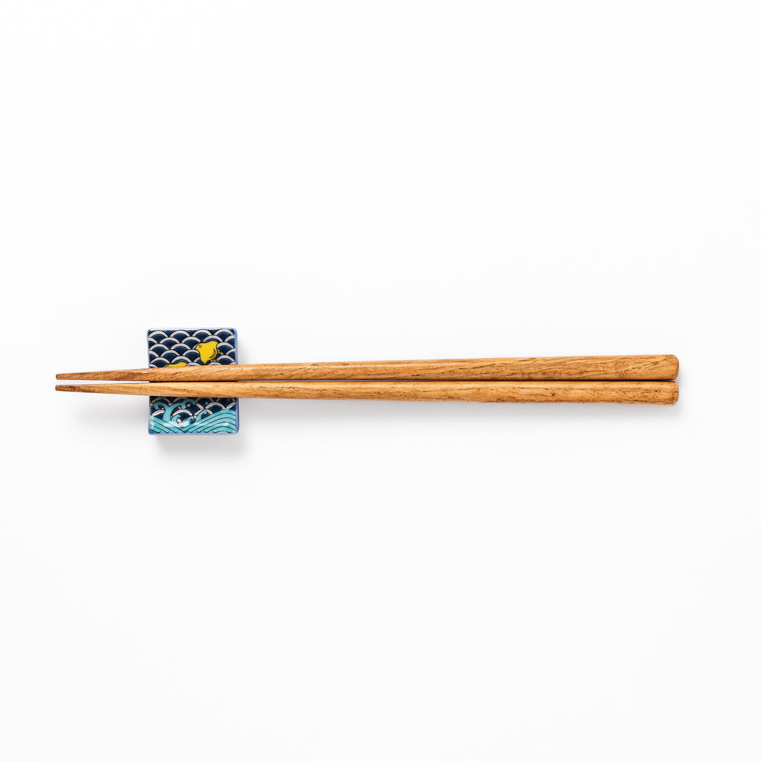 Rectangular Japanese ceramic chopstick rest decorated with a blue wave pattern and playful yellow shorebirds, adding charm and tradition to dining tables.