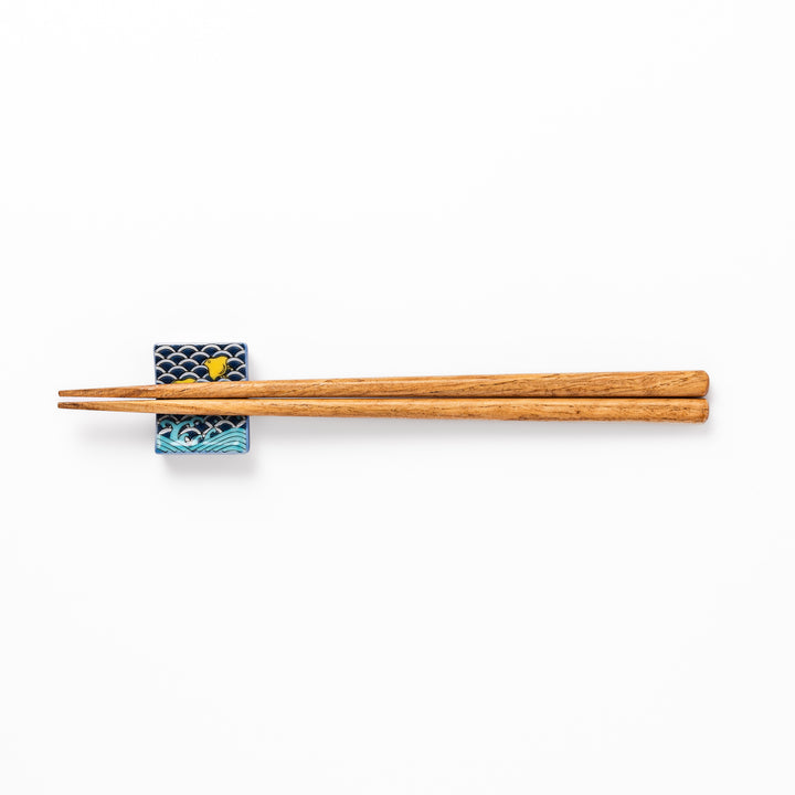 Rectangular Japanese ceramic chopstick rest decorated with a blue wave pattern and playful yellow shorebirds, adding charm and tradition to dining tables.